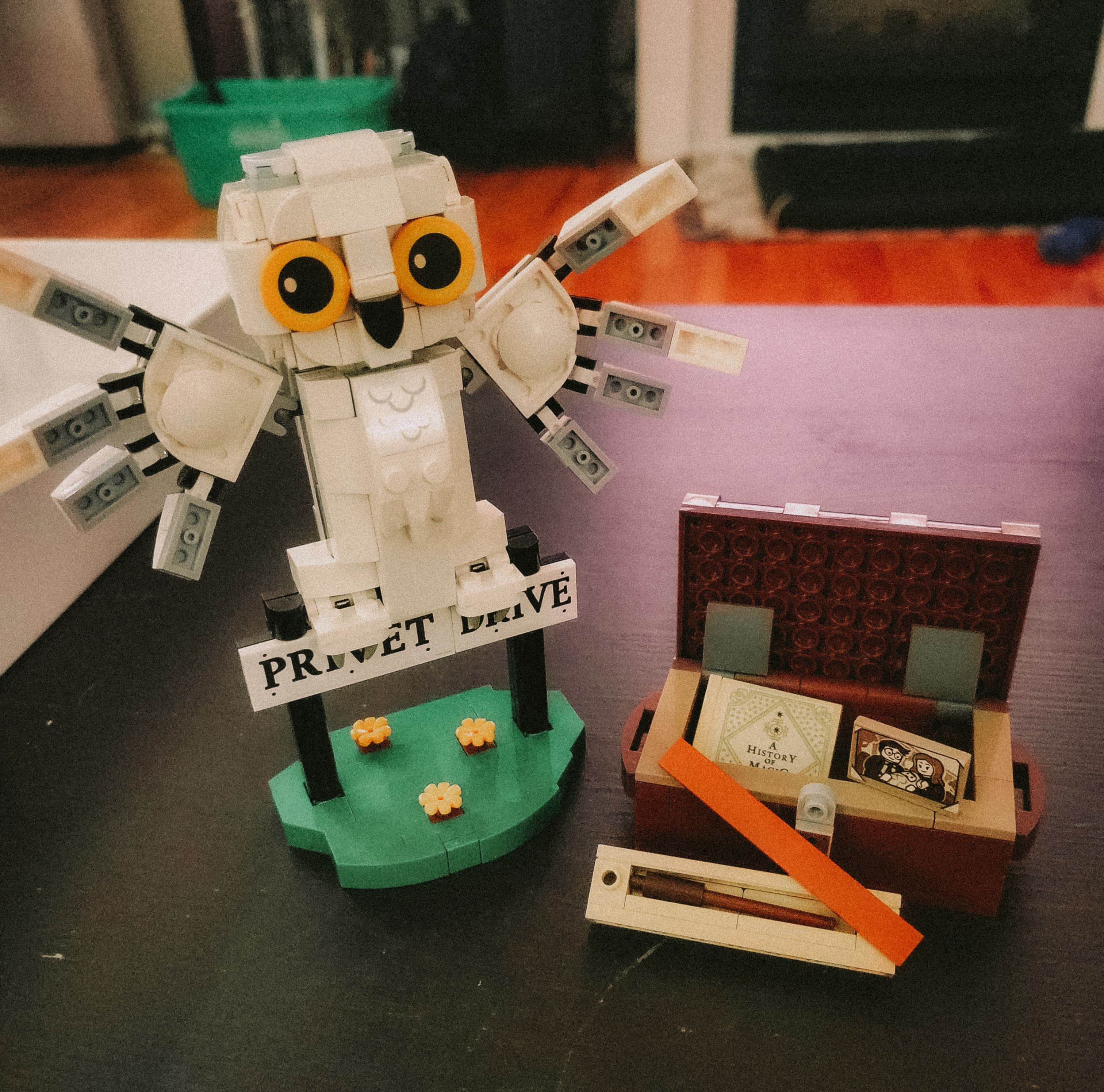 Completed LEGO set for "Hedwig at 4 Privet Drive (#76425)". The set is a white LEGO owl (Hedwig) alongside a chest containing Harry Potter's posessions: a broomstick, the textbook A History of Magic, and a photo of his friends.