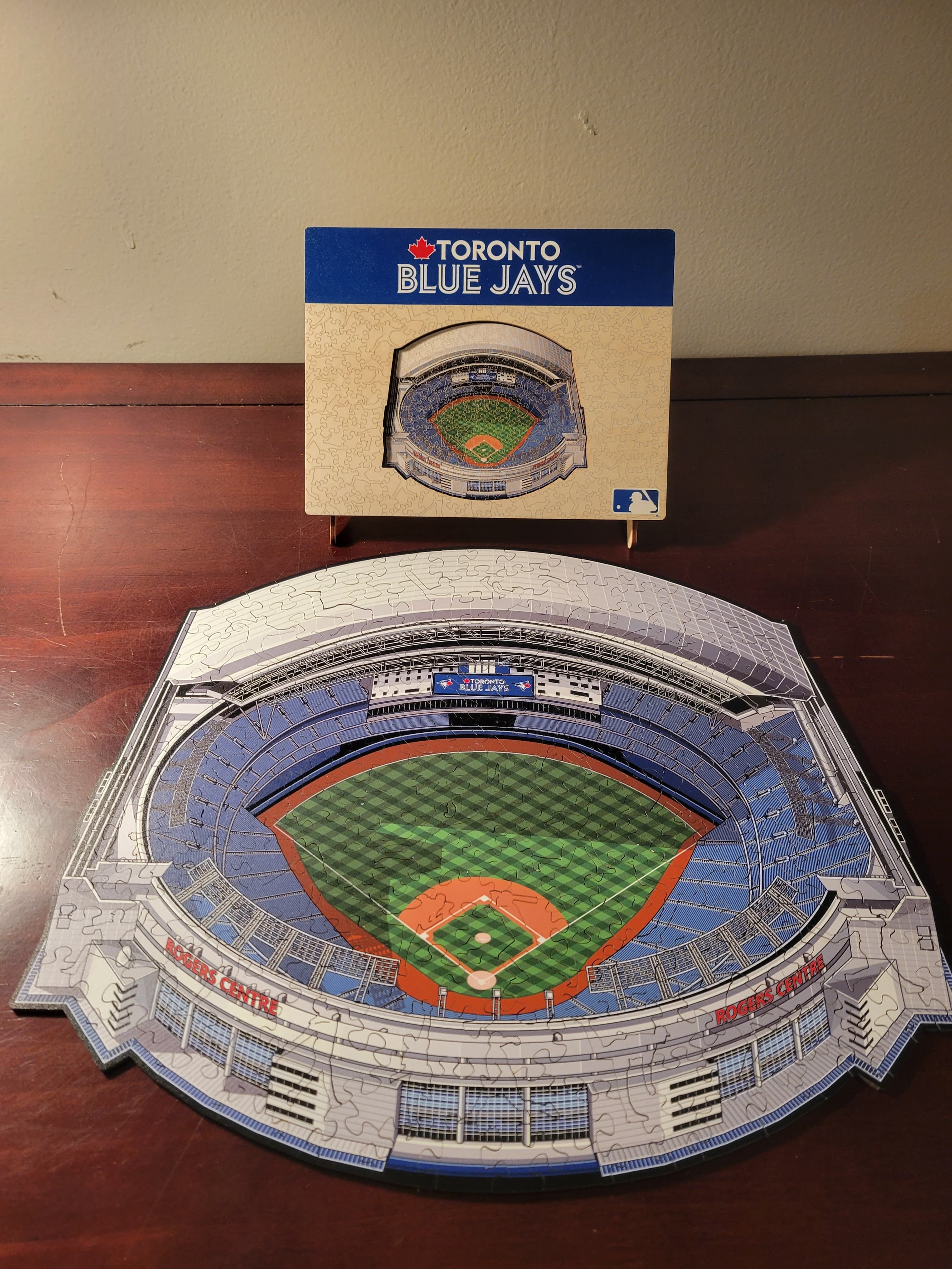 A completed puzzle depicting the Rogers Centre, home field of the Toronto Blue Jays. The field is hand drawn and not photorealistic. The box cover is standing behind the puzzle.