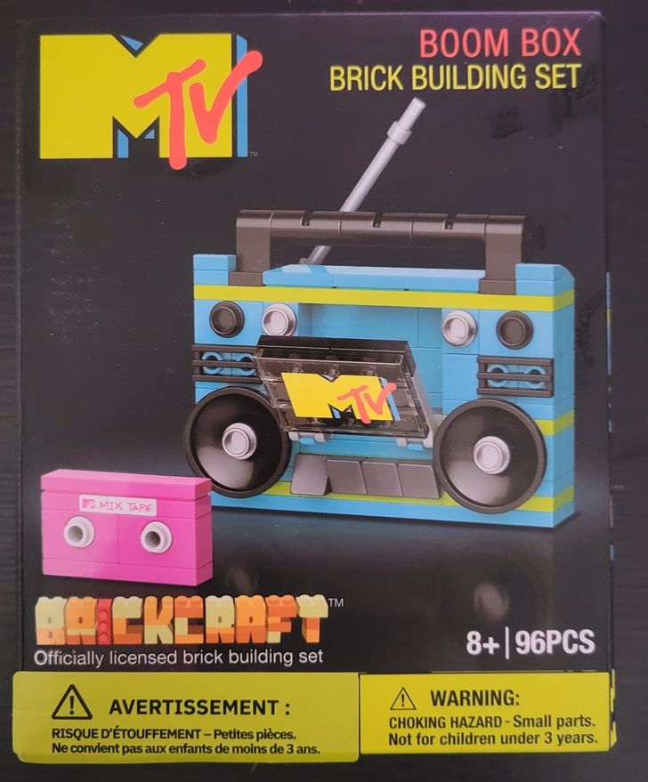 Front of a building toy by Brickcraft showing a boombox with the MTV logo with a small mixtape beside it. The set is called "MTV Boombox Brick Building Set".